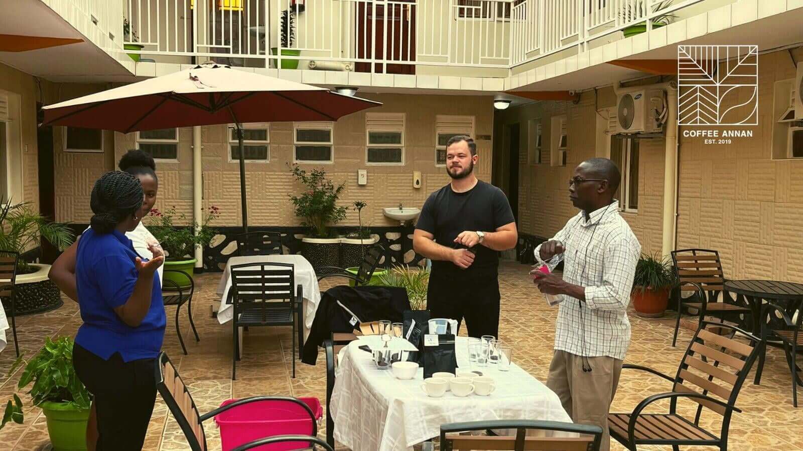 Drei Personen im Gespräch in einem offenen Innenhof mit Tischen – Austausch zwischen Partner:innen im Kontext des Direkthandels