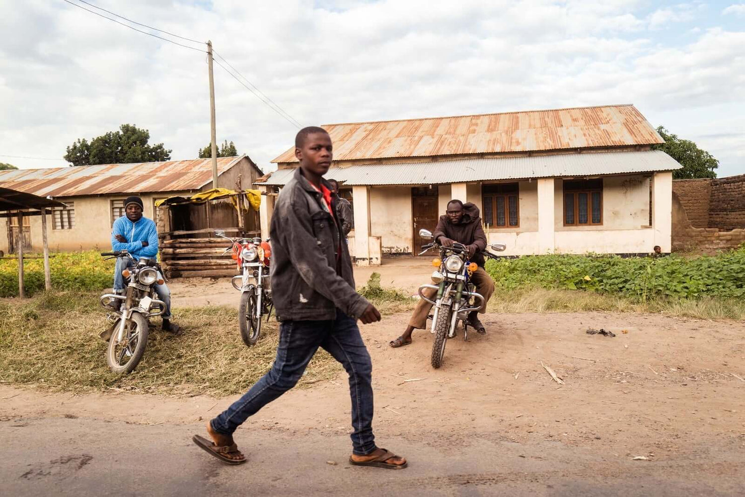 Männer mit Motorrädern vor Gebäuden in einer ländlichen Region Afrikas.